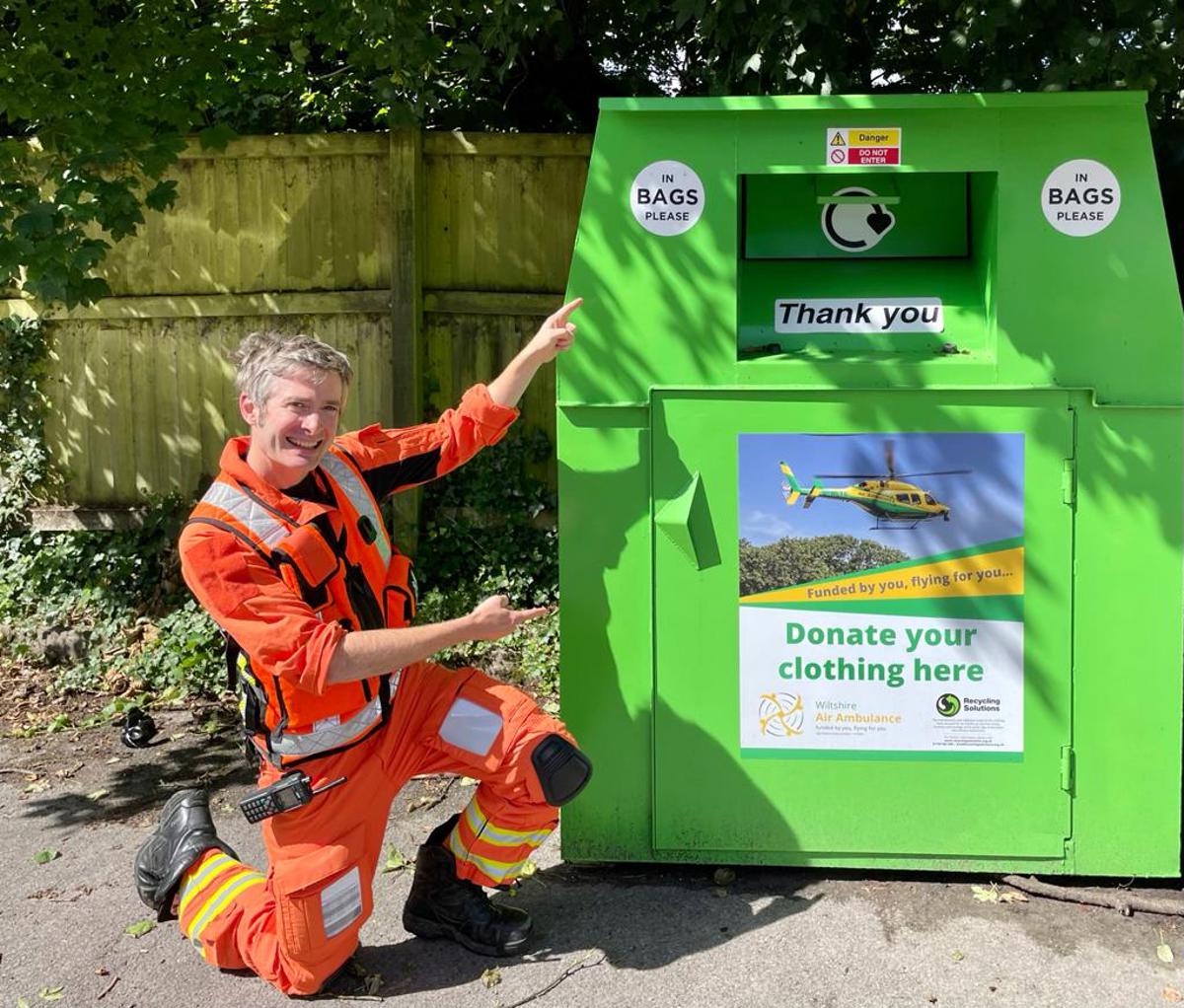 A doctor wearing an orange flight suit, crouched and pointing at a WAA green clothing bank A doctor wearing an orange flight suit, crouched and pointing at a WAA green clothing bank