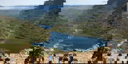 A sunny photo of walkers walking down Snowdon, overlooking a lake