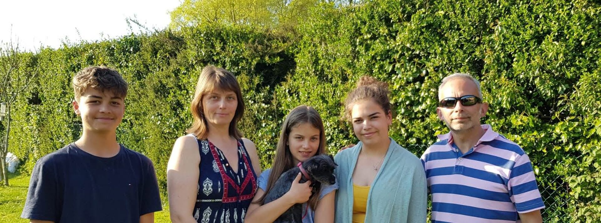 A family and their dog stood in a garden against a green hedge A family and their dog stood in a garden against a green hedge