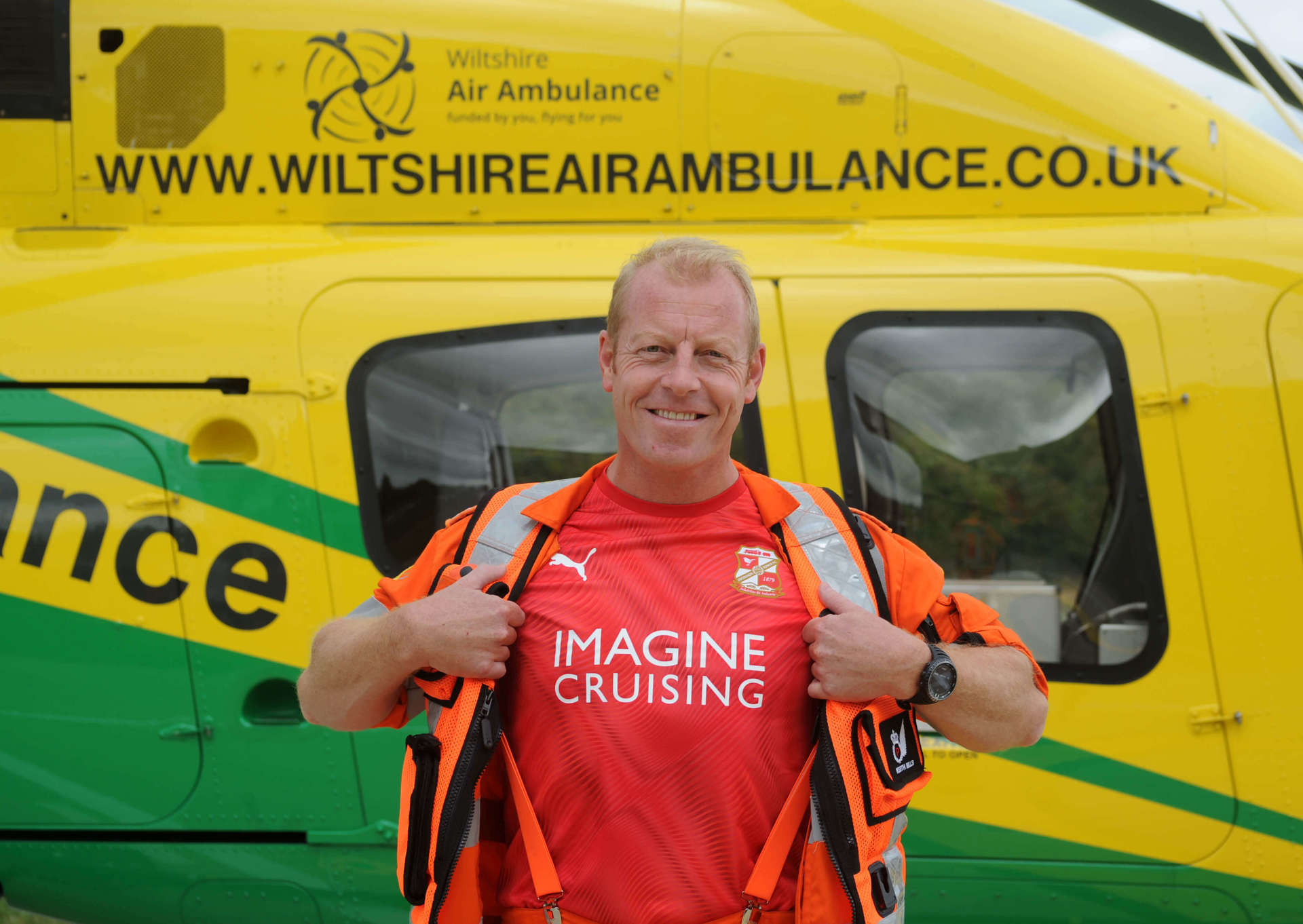 Critical care paramedic wearing a flight suit and Swindon Town Football shirt underneath stood in front of the Bell-429 helicopter. Critical care paramedic wearing a flight suit and Swindon Town Football shirt underneath stood in front of the Bell-429 helicopter.