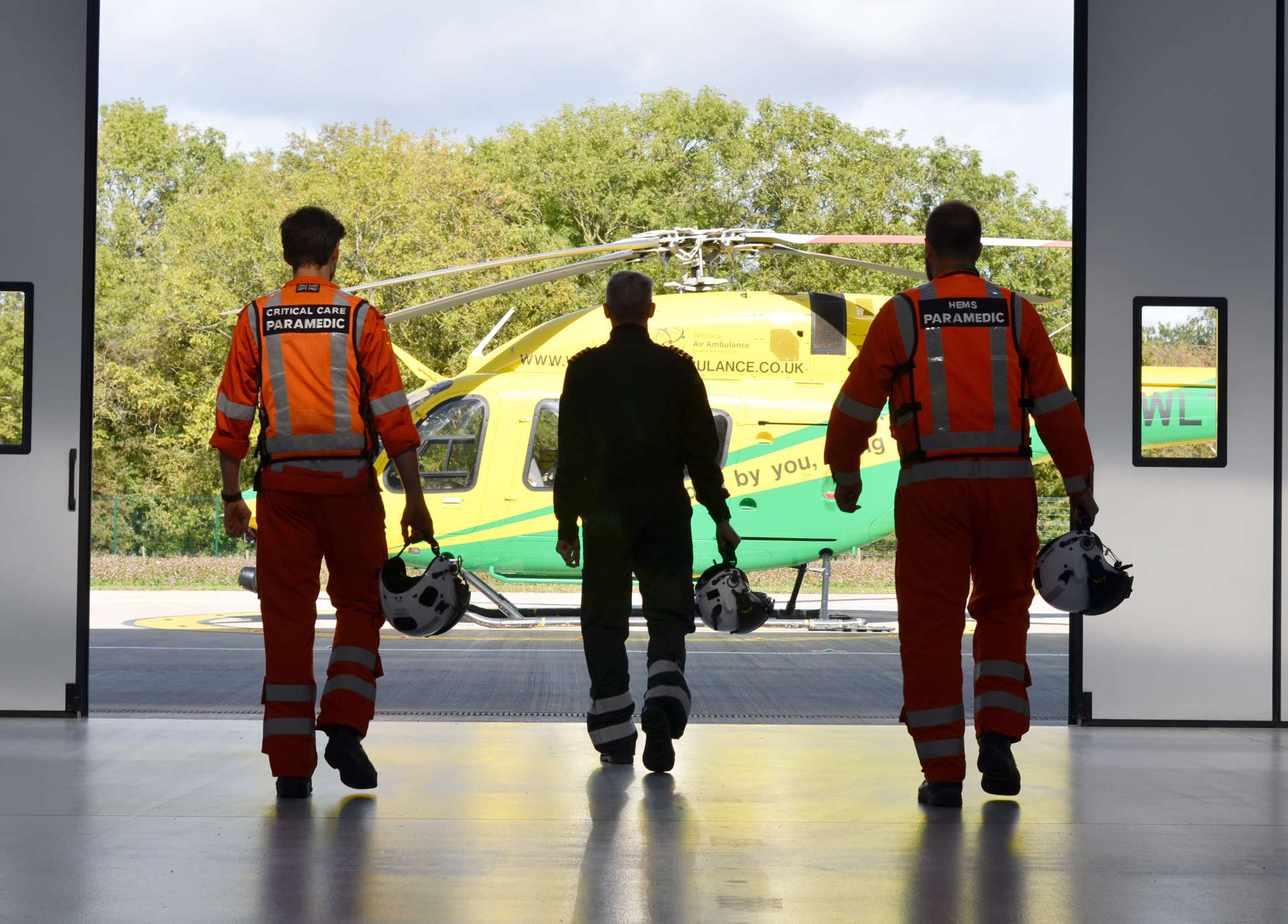 Two paramedics and a pilot walking towards the helicopter from inside the hangar. Two paramedics and a pilot walking towards the helicopter from inside the hangar.