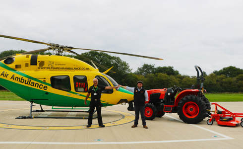 An orange Kubota tractor and trailer parked on the helipad next to the helicopter. There is a staff member from WAA and Howard & Sons handing over the keys. An orange Kubota tractor and trailer parked on the helipad next to the helicopter. There is a staff member from WAA and Howard & Sons handing over the keys.