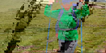 A person wearing a green raincoat and blue backpack, holding walking poles in the air