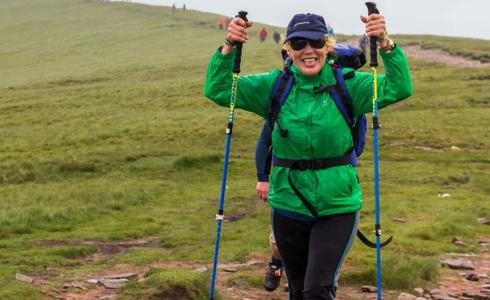 A person wearing a green raincoat and blue backpack, holding walking poles in the air A person wearing a green raincoat and blue backpack, holding walking poles in the air