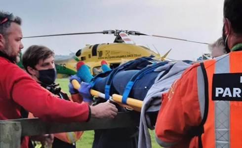 A patient being carried over a fence on a stretcher. The Bell 429 helicopter is in the background. A patient being carried over a fence on a stretcher. The Bell 429 helicopter is in the background.