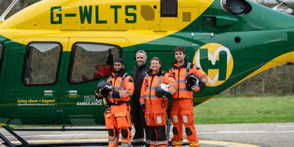 A group of air ambulance colleagues standing in front of a yellow and green helicopter