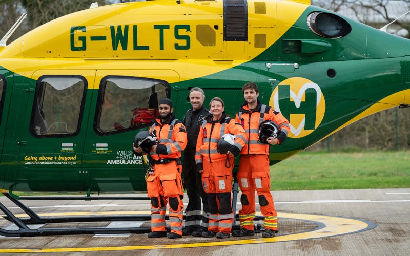 A group of air ambulance colleagues standing in front of a yellow and green helicopter A group of air ambulance colleagues standing in front of a yellow and green helicopter
