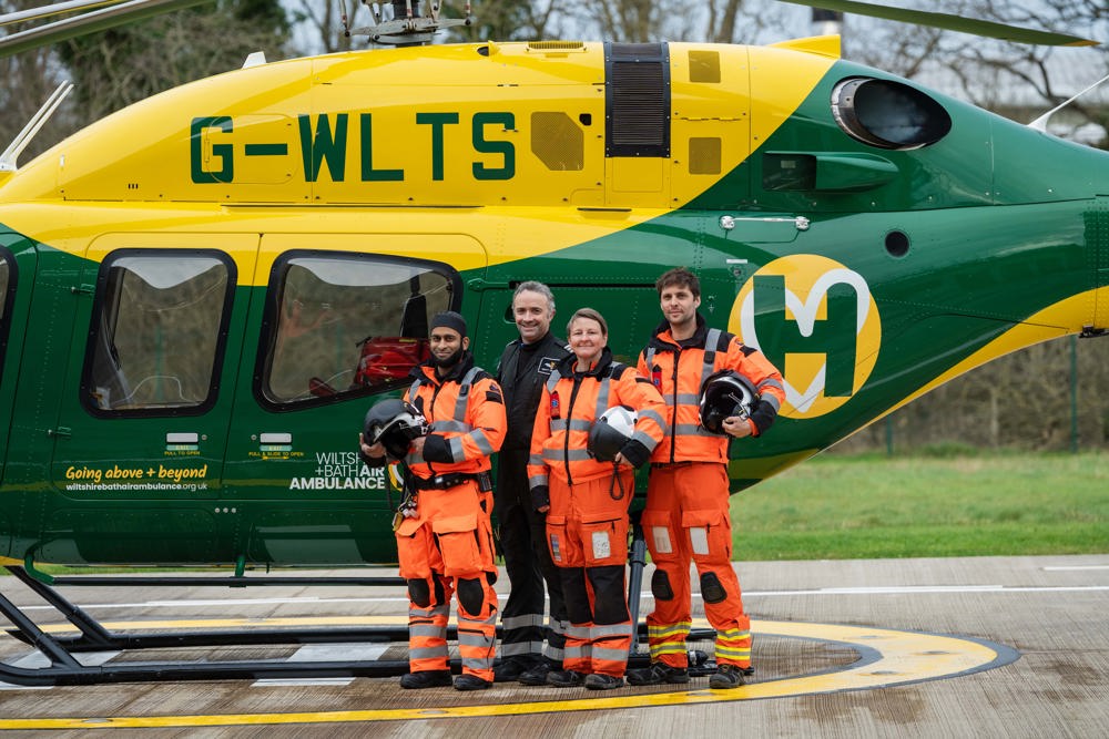 A group of air ambulance colleagues standing in front of a yellow and green helicopter