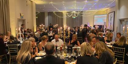 Black and gold themed charity ball. Groups of people wearing smart clothing, sitting on gold chairs around round tables Black and gold themed charity ball. Groups of people wearing smart clothing, sitting on gold chairs around round tables
