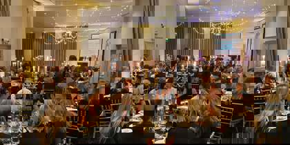 Black and gold themed charity ball. Groups of people wearing smart clothing, sitting on gold chairs around round tables Black and gold themed charity ball. Groups of people wearing smart clothing, sitting on gold chairs around round tables