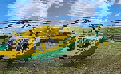 Yellow and green Wiltshire Air Ambulance helicopter landed in a field with white horse in the background