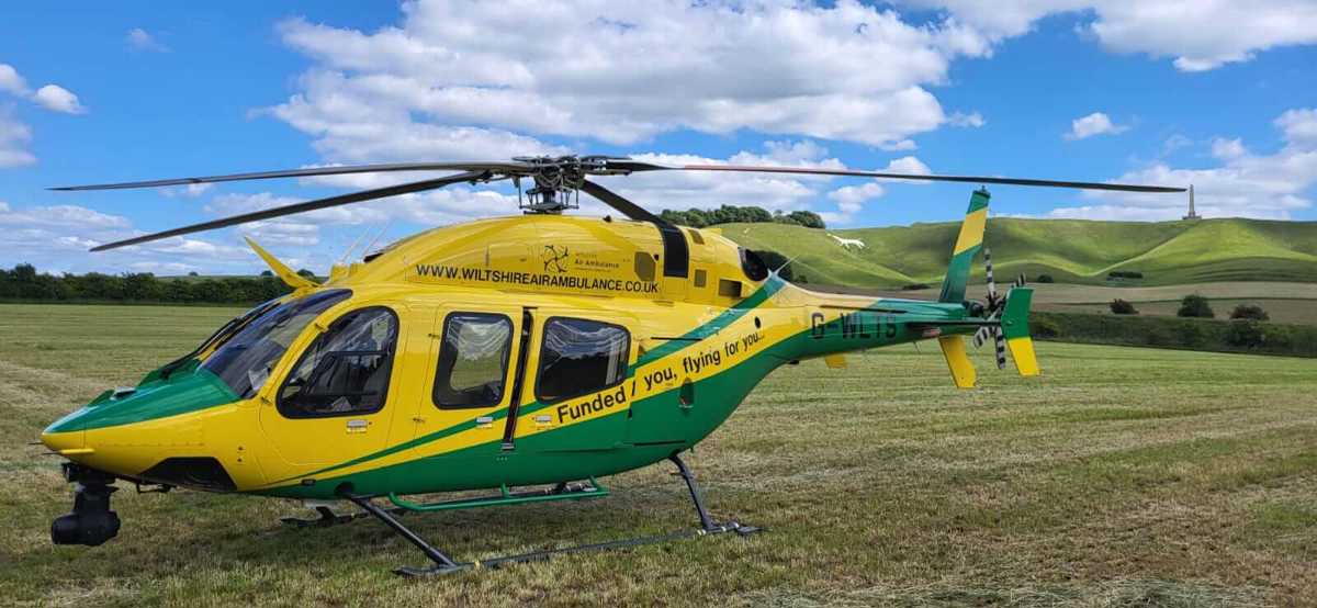 Yellow and green Wiltshire Air Ambulance helicopter landed in a field with white horse in the background Yellow and green Wiltshire Air Ambulance helicopter landed in a field with white horse in the background