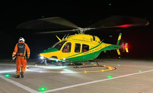 A paramedic wearing an orange flight suit walking towards a yellow and green helicopter A paramedic wearing an orange flight suit walking towards a yellow and green helicopter