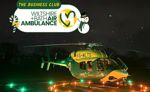 The Bell-429 helicopter at night, sat on a lit helipad with yellow and green lights on.