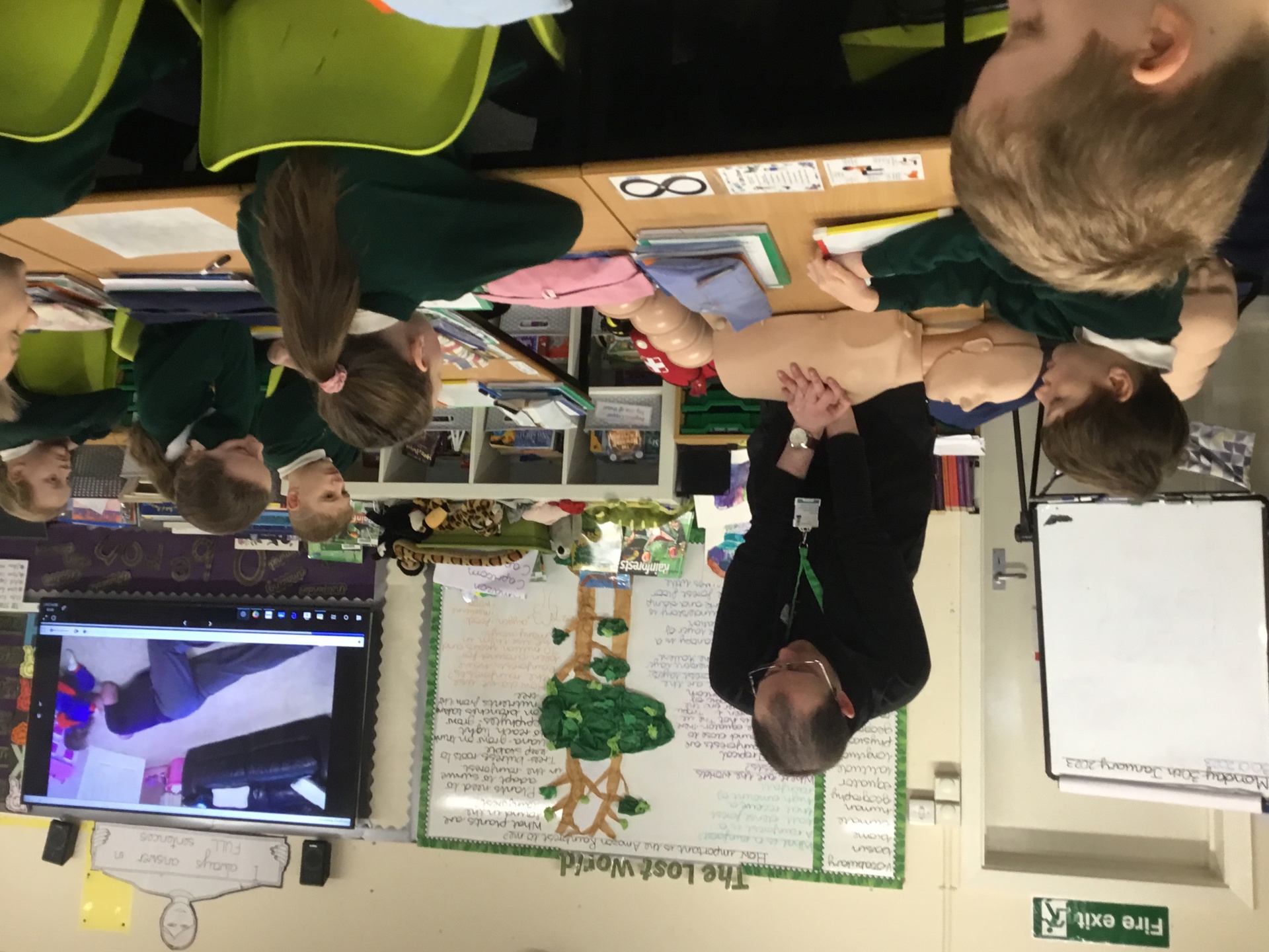 A man performing CPR on a manikin, with school children watching on A man performing CPR on a manikin, with school children watching on