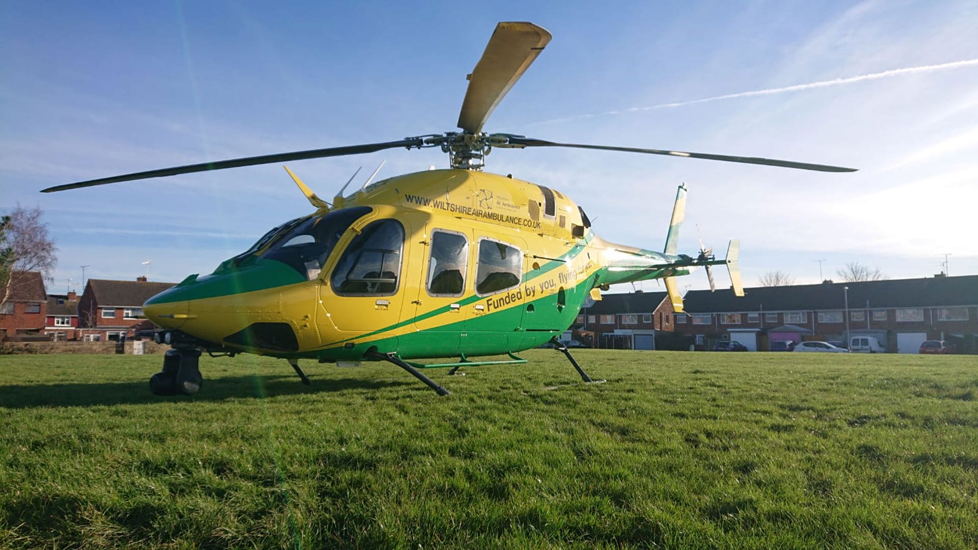 A yellow and green helicopter landed on a green in Swindon, with houses behind A yellow and green helicopter landed on a green in Swindon, with houses behind