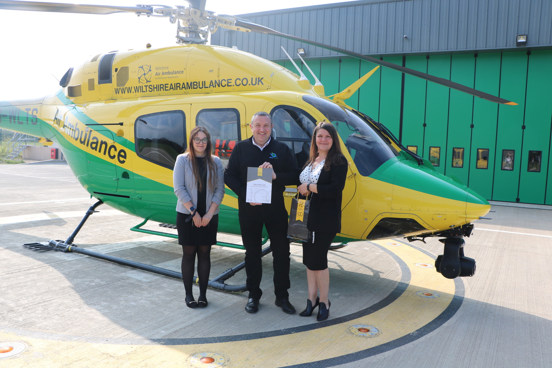 Matt Goodall and Office Evolution colleagues holding 100 club branded certificate and gift bag, standing in front of the helicopter Matt Goodall and Office Evolution colleagues holding 100 club branded certificate and gift bag, standing in front of the helicopter