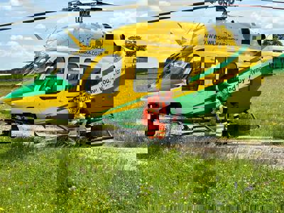 A photo of a paramedic and pilot smiling at the camera whilst perching on the step of the Wiltshire Air Ambulance's yellow and green helicopter A photo of a paramedic and pilot smiling at the camera whilst perching on the step of the Wiltshire Air Ambulance's yellow and green helicopter