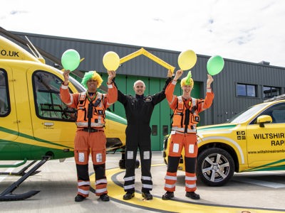 Paramedic Rich Miller wearing a yellow and green curly wig and holding yellow and green balloons, Rob Backus holding yellow Team WAA cheer sticks and Craig Wilkins wearing a yellow and green mohawk wig and holding yellow and green balloons Paramedic Rich Miller wearing a yellow and green curly wig and holding yellow and green balloons, Rob Backus holding yellow Team WAA cheer sticks and Craig Wilkins wearing a yellow and green mohawk wig and holding yellow and green balloons