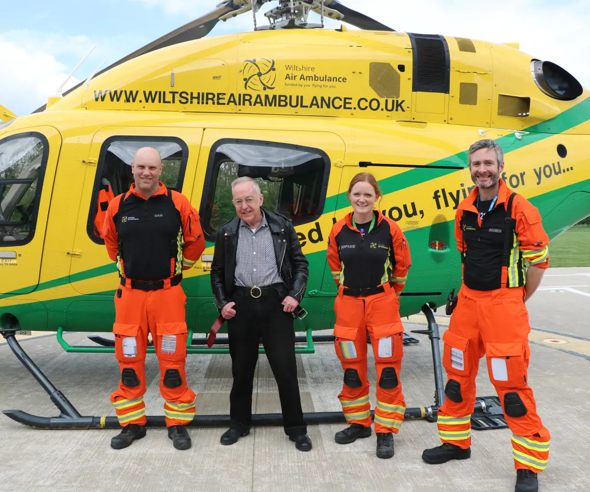 Patient Martyn Dormer standing in front of the helicopter with critical care paramedics Dan and Sophie, and doctor Reuben who are wearing orange flight suits, Patient Martyn Dormer standing in front of the helicopter with critical care paramedics Dan and Sophie, and doctor Reuben who are wearing orange flight suits,