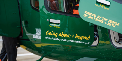 Yellow text with going above + beyond and funded by the people of wiltshire + bath on the doors of a green helicopter