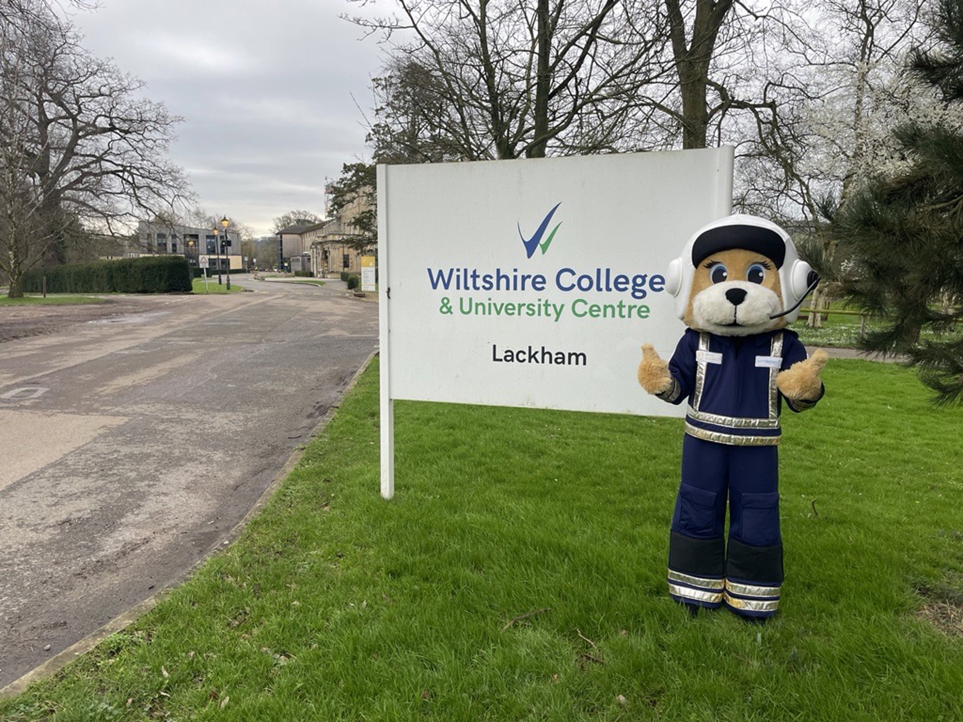 A photo of a bear mascot standing with a sign saying Wiltshire College A photo of a bear mascot standing with a sign saying Wiltshire College