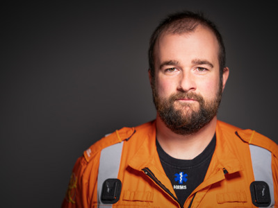 Critical care paramedic James Hubbard headshot photo wearing an orange flight suit on a black background. Critical care paramedic James Hubbard headshot photo wearing an orange flight suit on a black background.