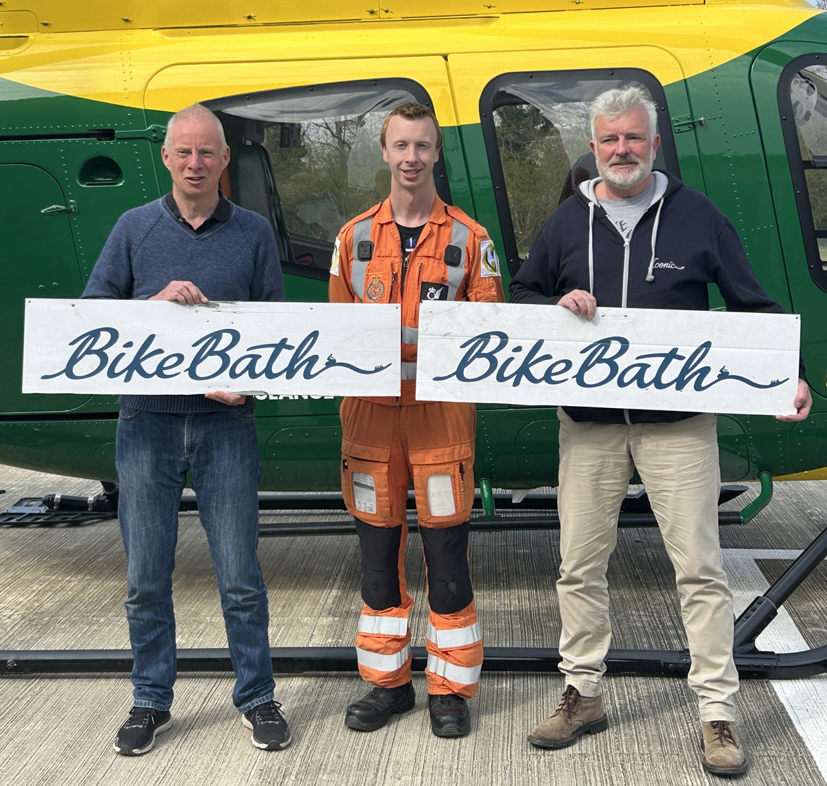 Three men holding Bike Bath banners in front of a yellow and green helicopter Three men holding Bike Bath banners in front of a yellow and green helicopter