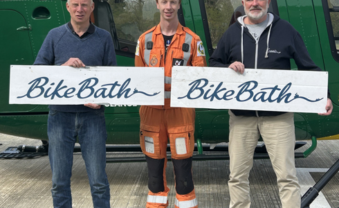 Three men holding Bike Bath banners in front of a yellow and green helicopter Three men holding Bike Bath banners in front of a yellow and green helicopter