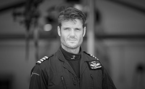 A black and white photograph of a pilot stood in front of the helicopter wearing a flight suit. A black and white photograph of a pilot stood in front of the helicopter wearing a flight suit.