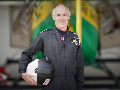 Pilot Rob in black flight suit, holding flight helmet with Wiltshire Air Ambulance's helicopter in the background Pilot Rob in black flight suit, holding flight helmet with Wiltshire Air Ambulance's helicopter in the background