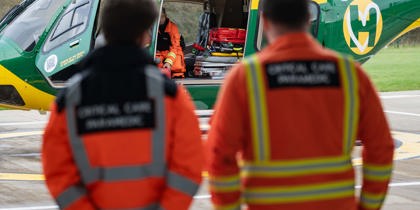 The back of orange jackets, with a yellow and green helicopter in the background