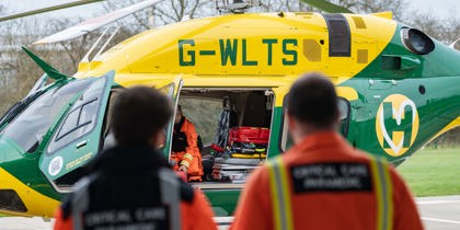 The back of orange jackets, with a yellow and green helicopter in the background
