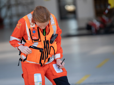 Paramedic Sophie Holt wearing orange flight suit and taking notes on leg pad Paramedic Sophie Holt wearing orange flight suit and taking notes on leg pad