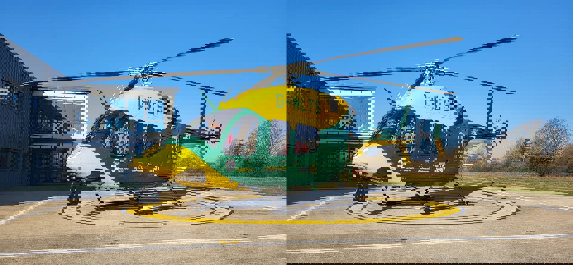 Yellow and green helicopter on helipad with blue sky behind