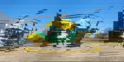 Yellow and green helicopter on helipad with blue sky behind Yellow and green helicopter on helipad with blue sky behind