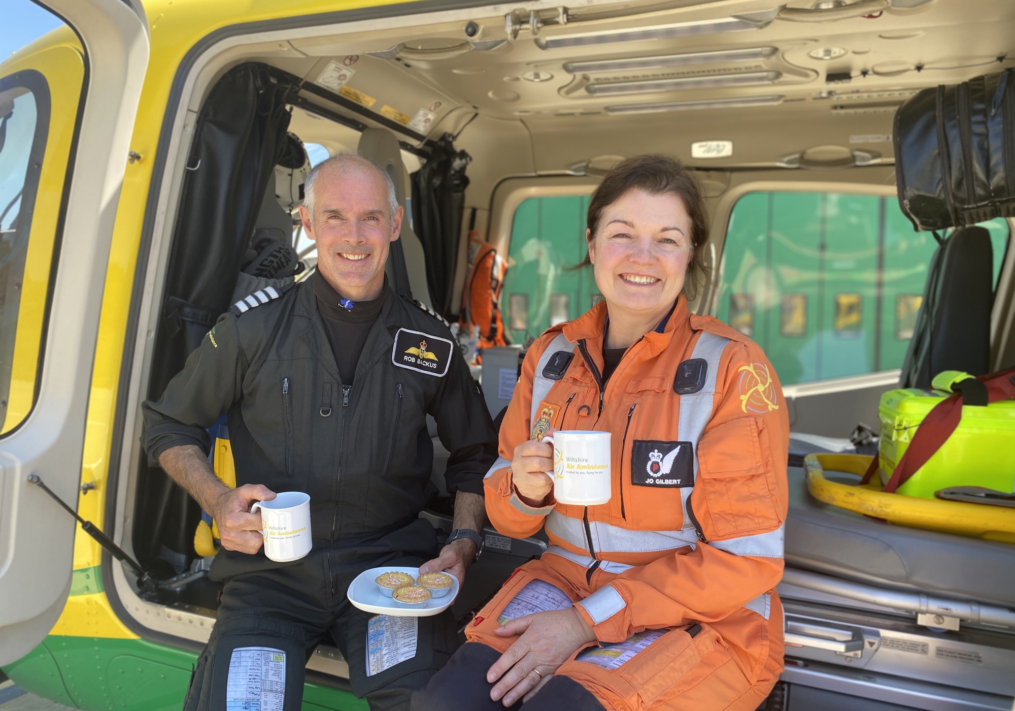 Pilot Rob and paramedic Jo posing with cakes and mugs whilst sat in Wiltshire Air Ambulance's helicopter Pilot Rob and paramedic Jo posing with cakes and mugs whilst sat in Wiltshire Air Ambulance's helicopter