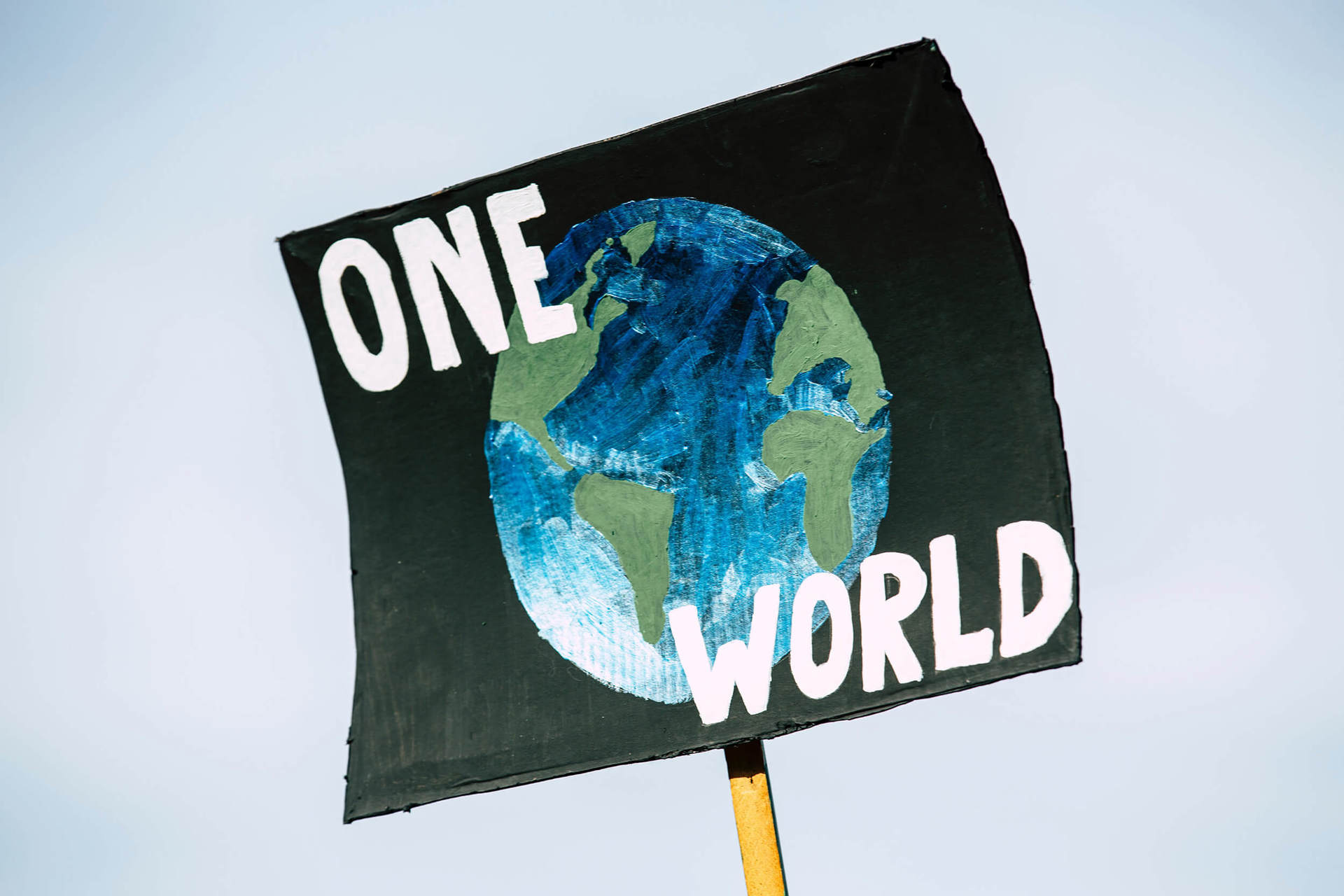 A handmade sign showing a painting of the earth with 'One World' in white paint A handmade sign showing a painting of the earth with 'One World' in white paint
