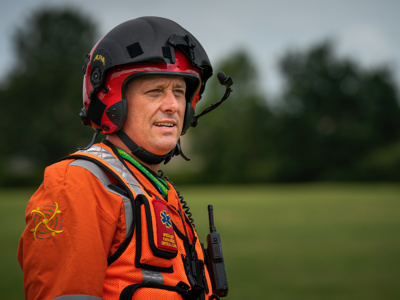 Paramedic Rich Miller wearing a red flight helmet and orange flight suit, with WAA avatar on the sleeve Paramedic Rich Miller wearing a red flight helmet and orange flight suit, with WAA avatar on the sleeve