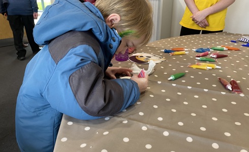 A boy wearing a blue and black jacket, with green glitter face paint, decorating a biscuit A boy wearing a blue and black jacket, with green glitter face paint, decorating a biscuit