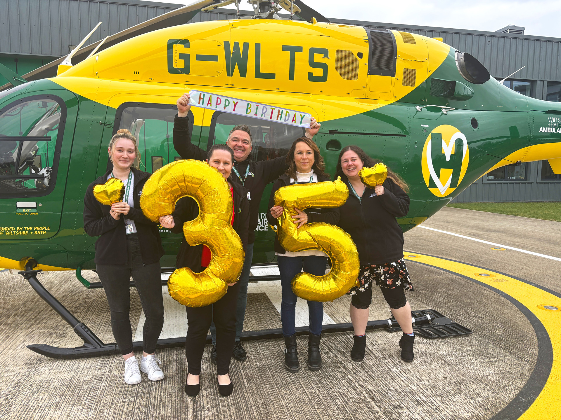 team holding a large gold 3 and 5 balloon